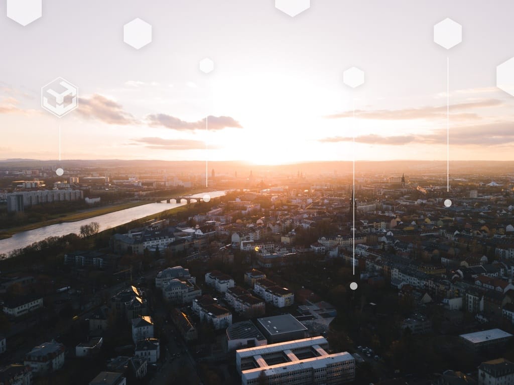 Luftaufnahme einer Stadt bei Sonnenuntergang, durchsetzt mit weißen sechseckigen Symbolen.
