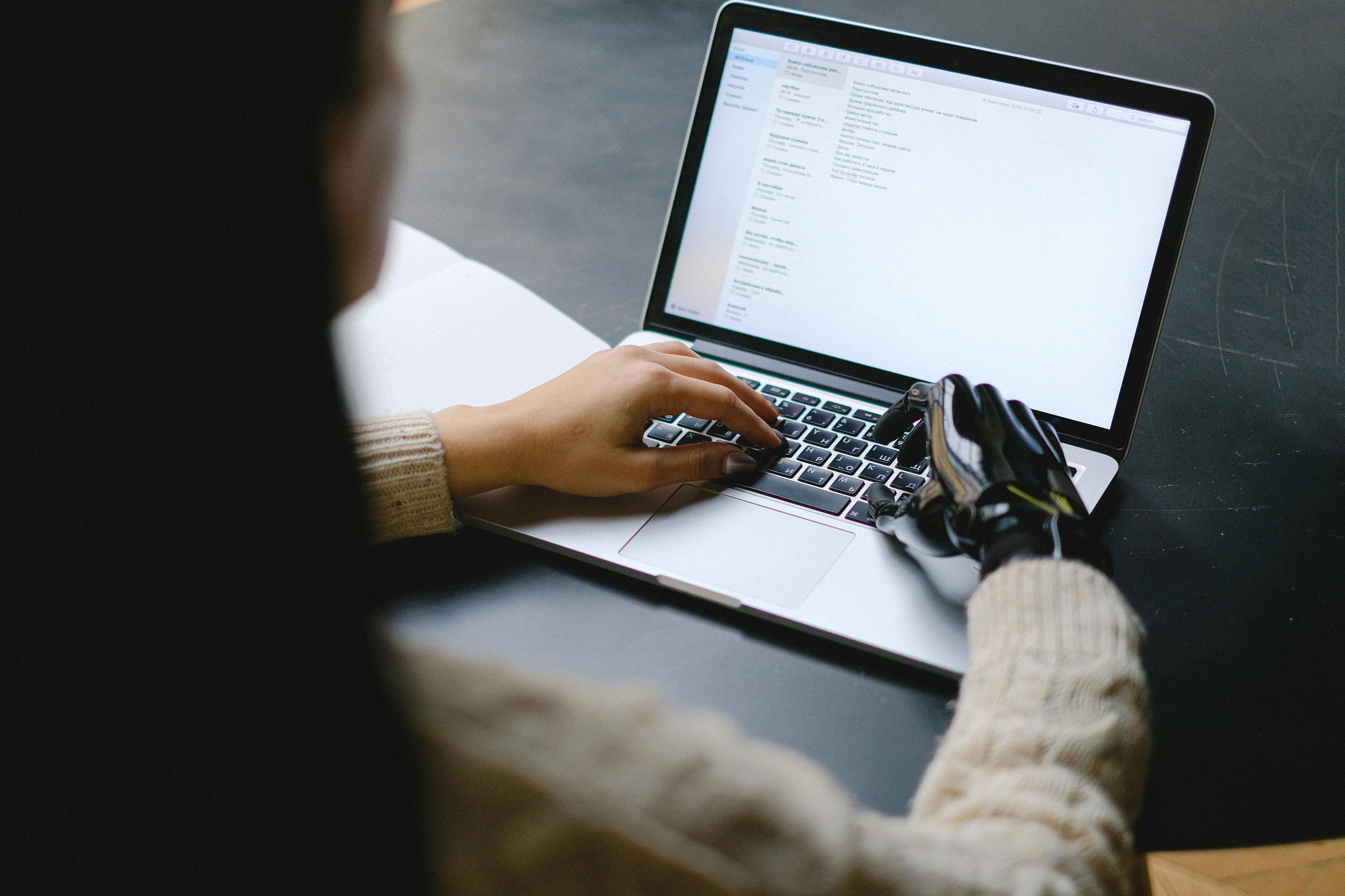 A woman with a prosthetic hand on her right arm is sitting at a laptop