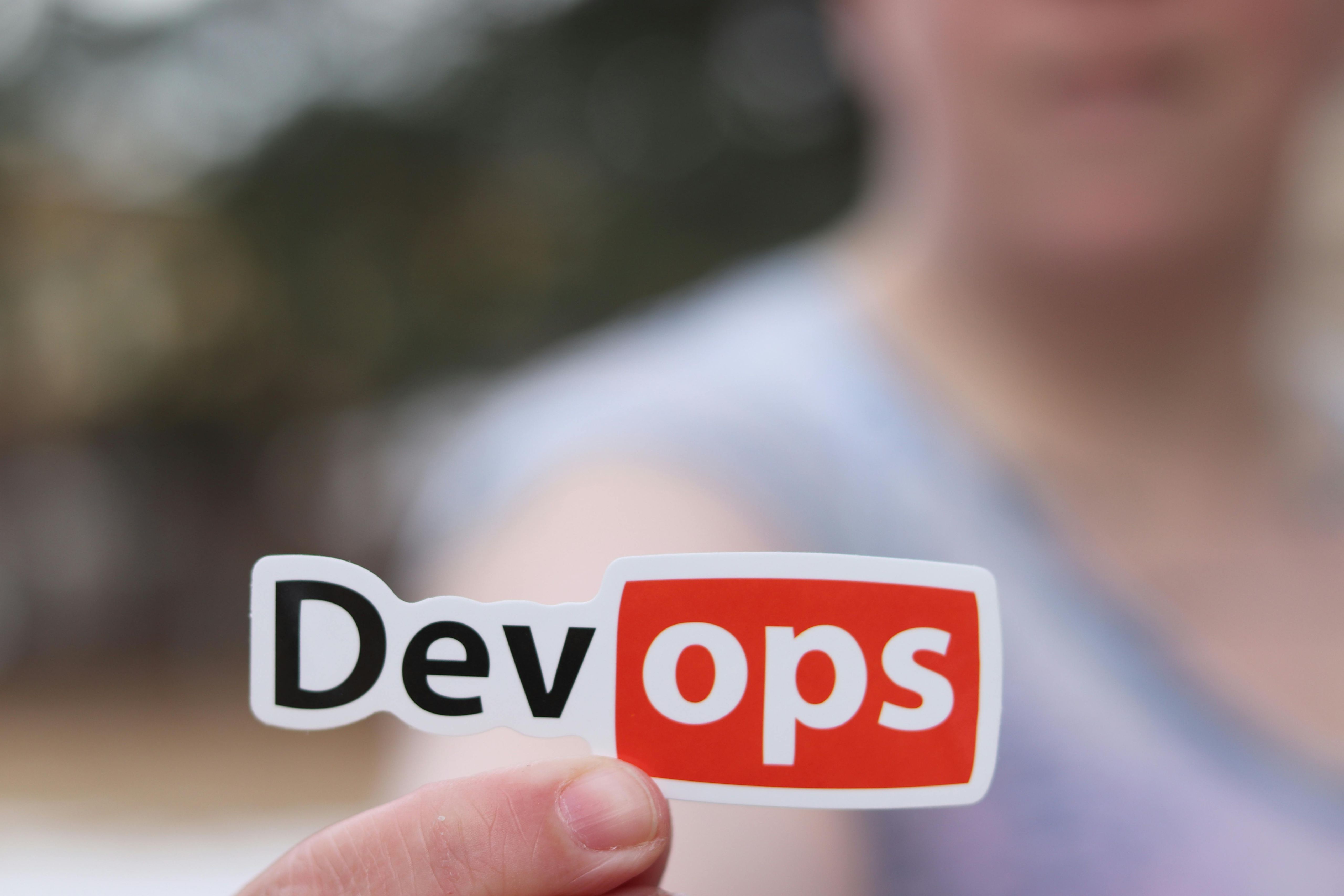 Eine Person hällt einen Sticker mit dem Schriftzug "Dev-ops" in der Hand